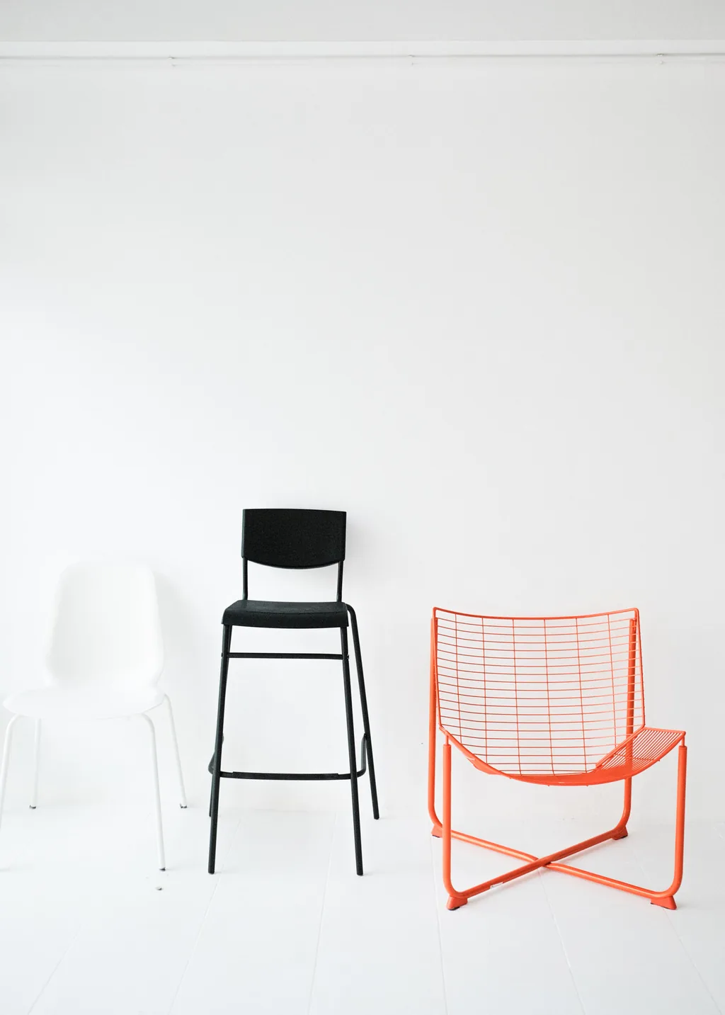 Black bar stool and orange wire chair on the white floor
