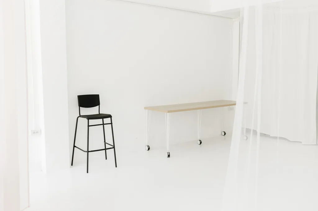 Black bar stool beside a white table on the bright studio floor