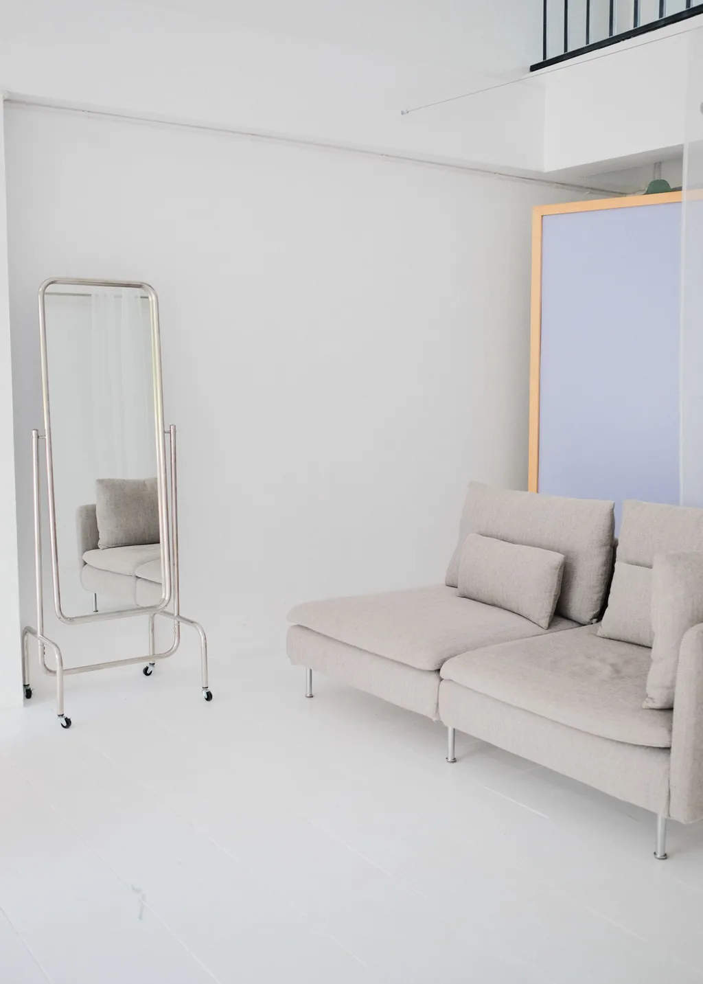 Floor mirror beside a grey sofa and lilac backdrop