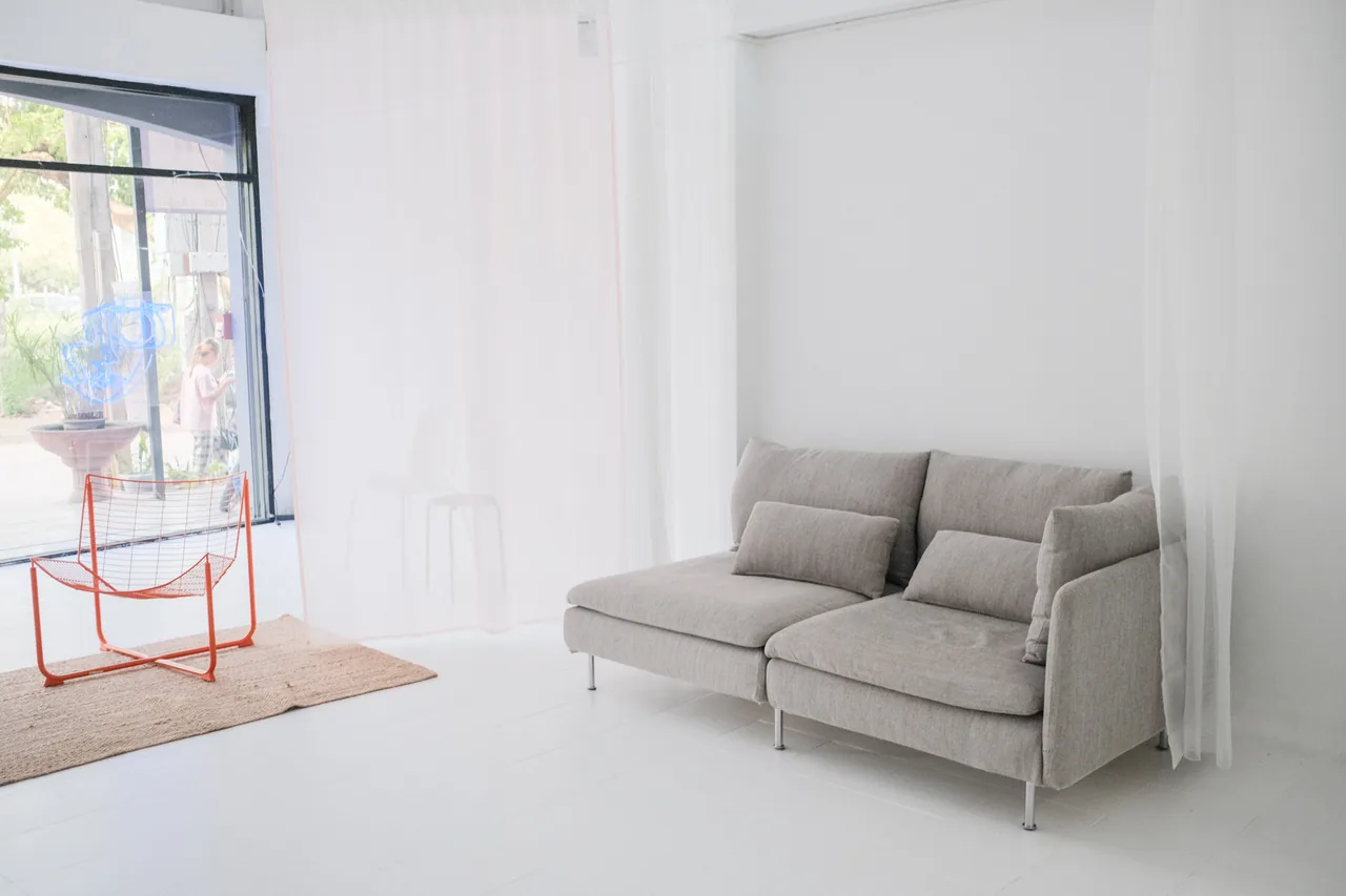 Grey sofa and orange wire chair beside the tall windows of the natural light studio