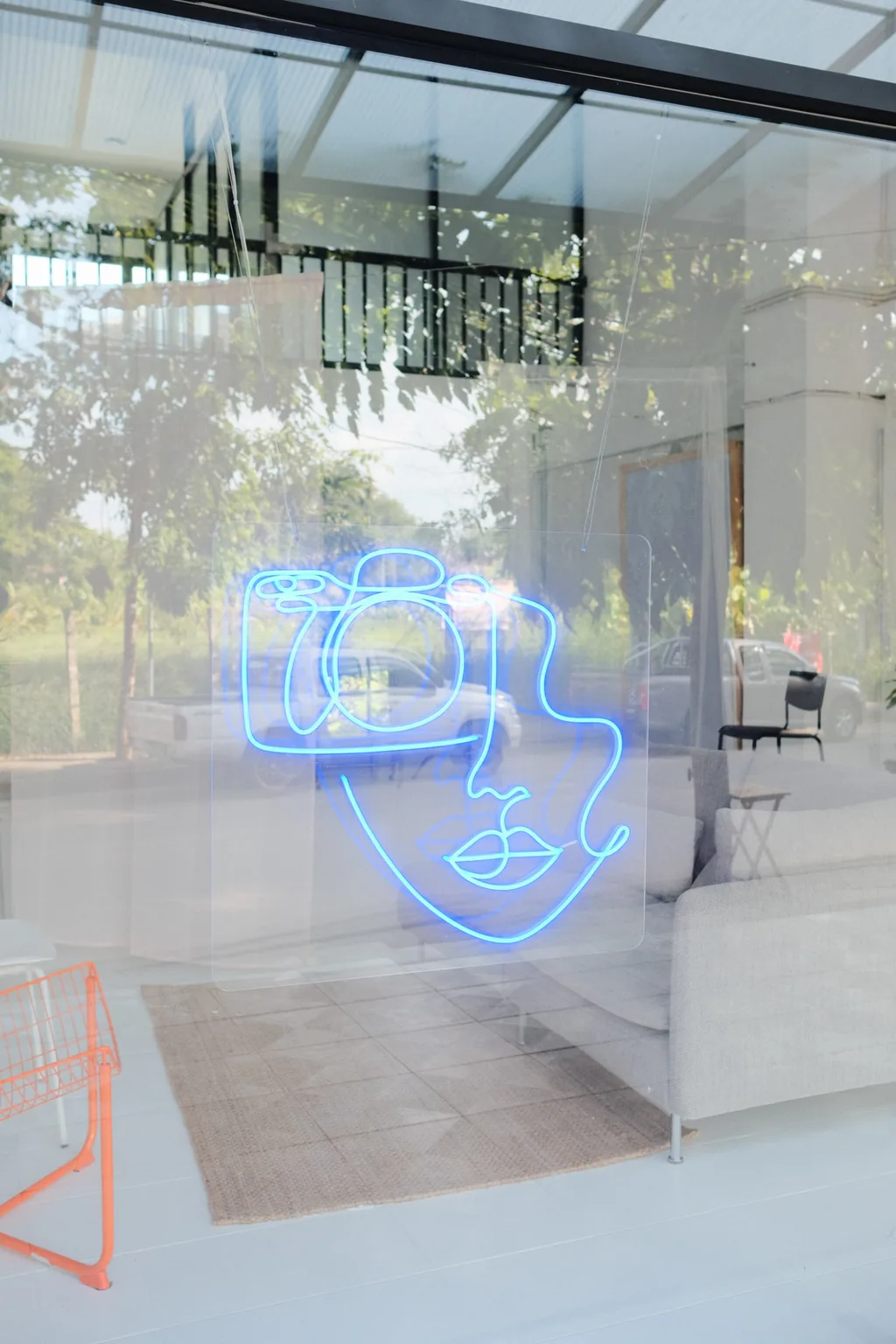 Blue neon camera logo on the studio window with trees outside