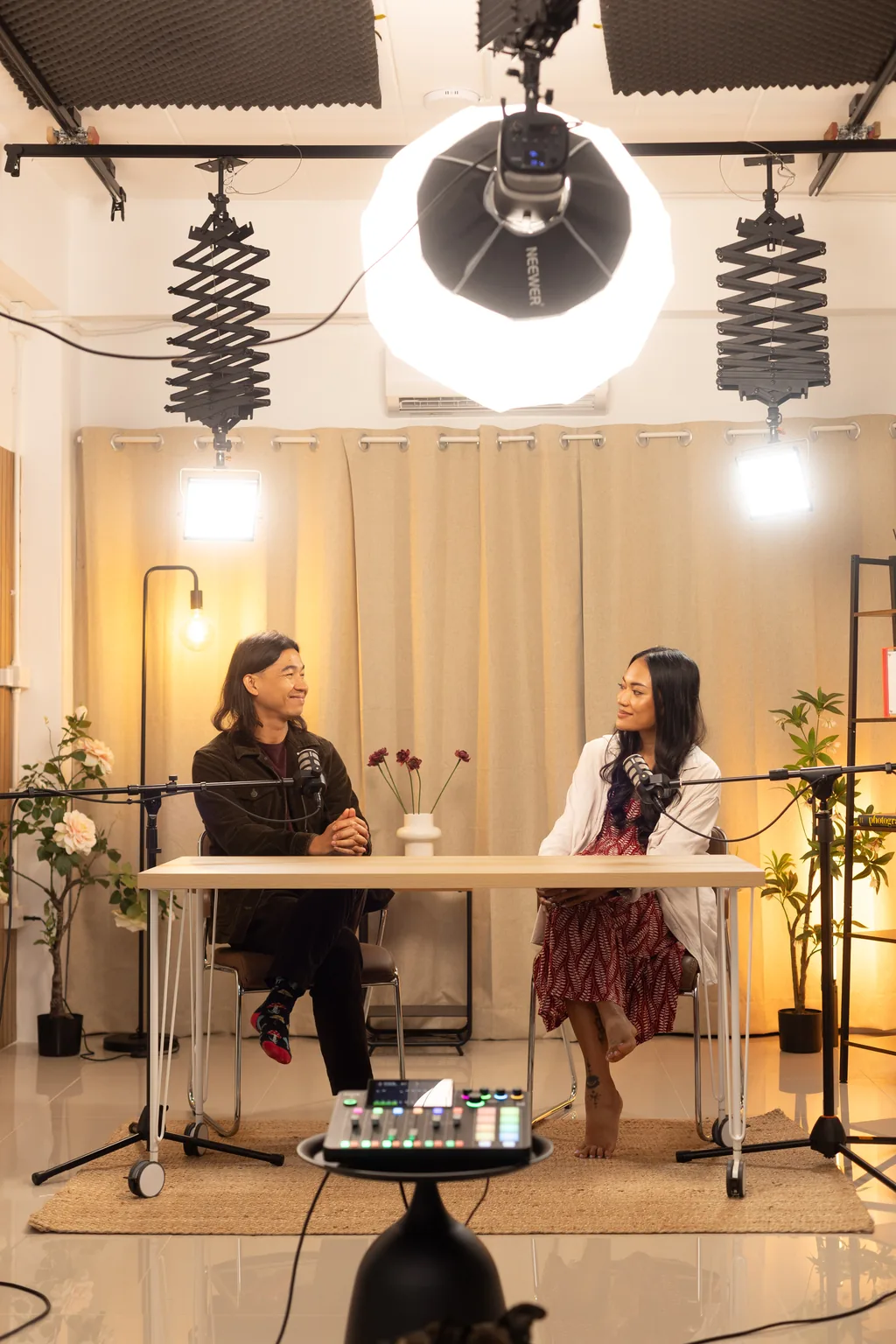 Two guests recording at a desk under a ring light and studio lights